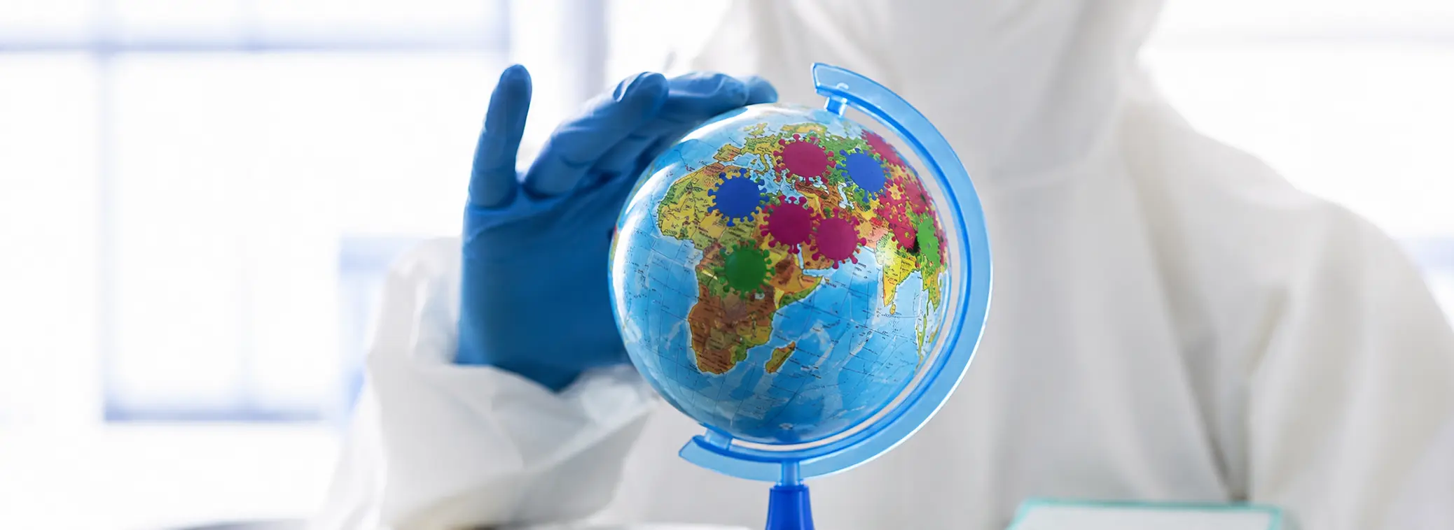 Scientist in lab coat and blue gloves holding a globe with virus icons, symbolizing global impact of AI in pharmaceutical research and drug discovery