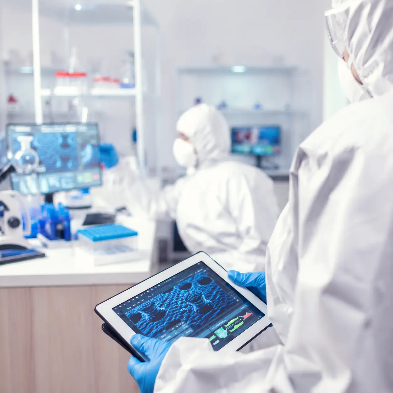 Scientist in lab coat and gloves holding a tablet displaying molecular data in a modern pharmaceutical laboratory, summarizing AI applications in drug discovery